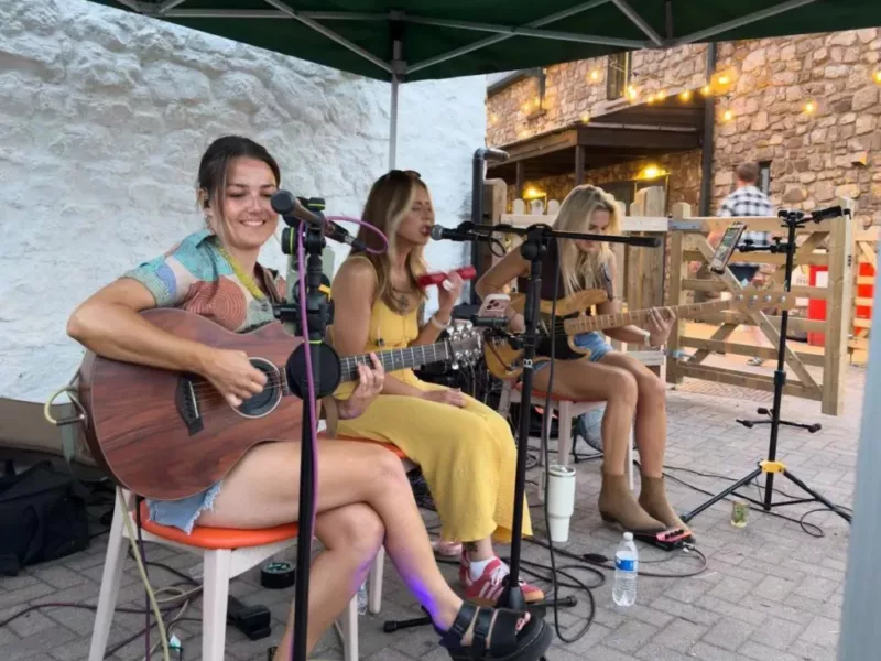 three women sat on chairs play guitars and sing