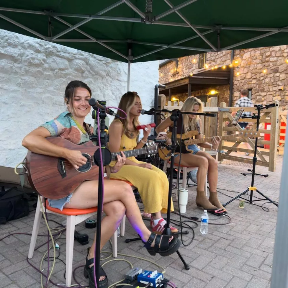 three women sat on chairs play guitars and sing
