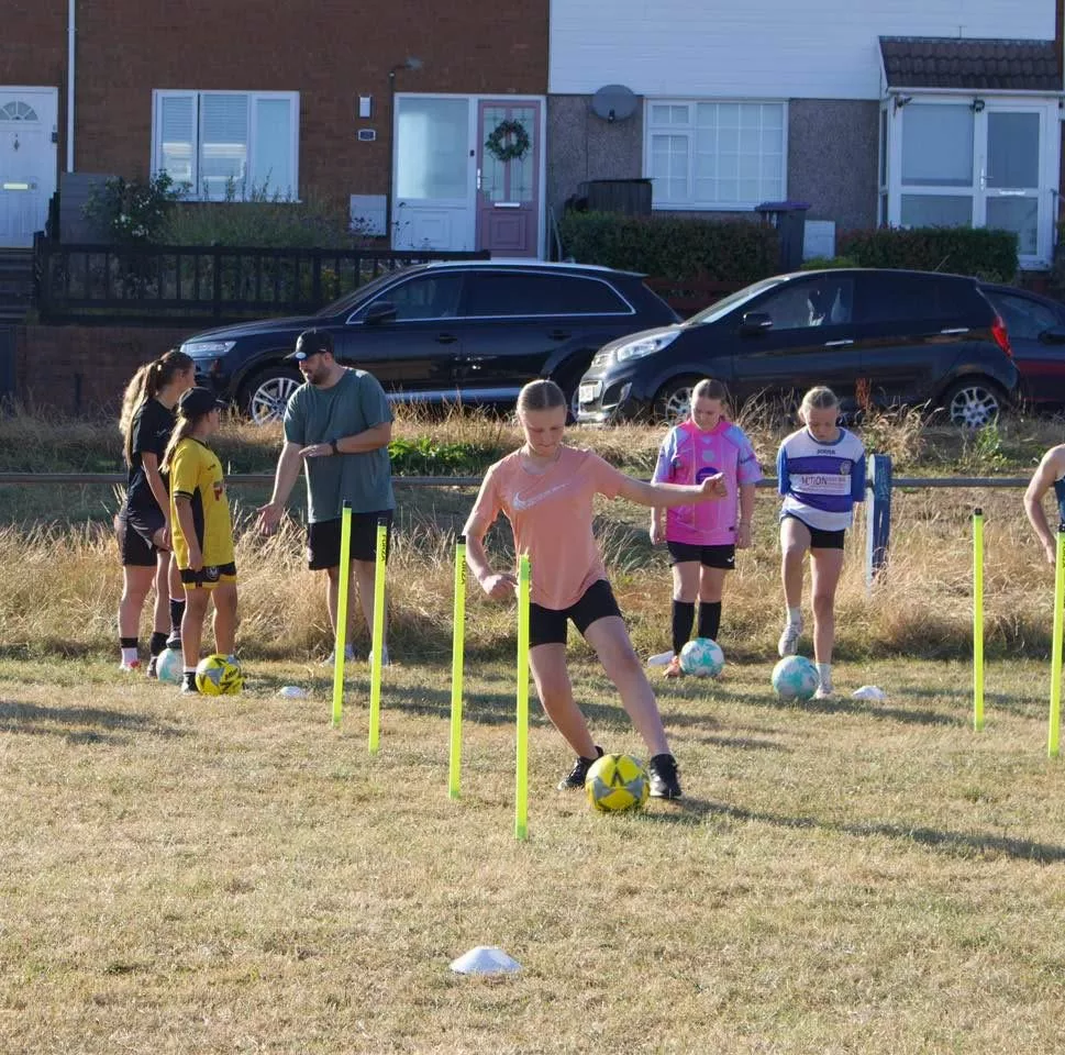 a girl dribbling a football through poles