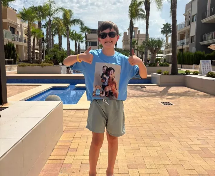 a young boy stood by a pool in the sun