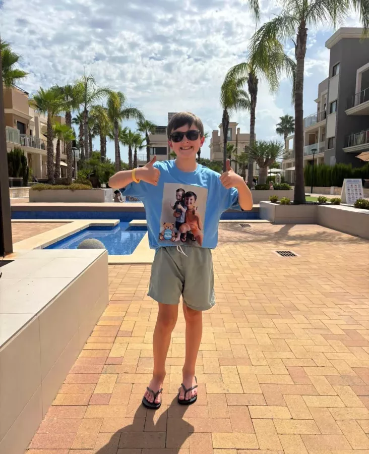 a young boy stood by a pool in the sun