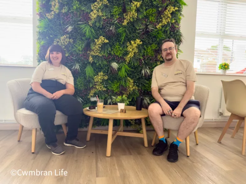 a man and a woman sitting at a table in front of a wall of artificial grass