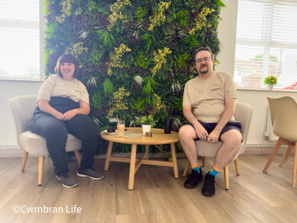 a man and a woman sitting at a table in front of a wall of artificial grass