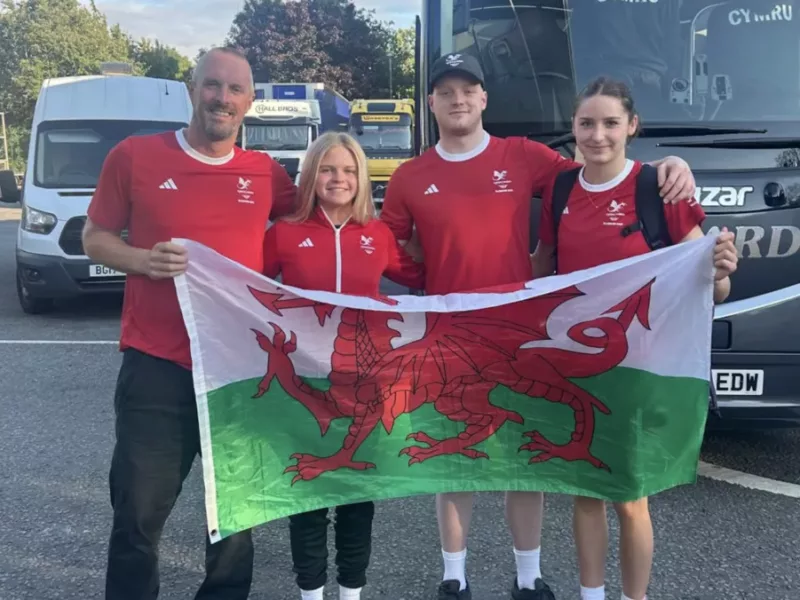 two men and two women hold a wales flag stood in front of a bus