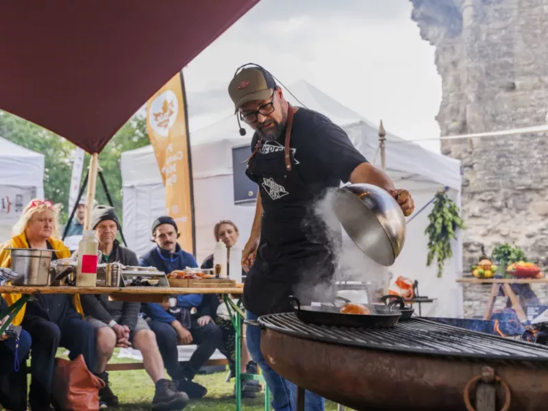 a man cooks on a bbq watched by a group of people