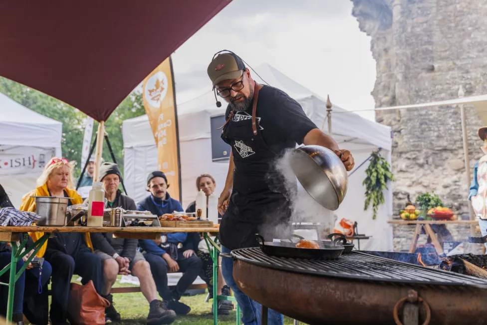 a man cooks on a bbq watched by a group of people