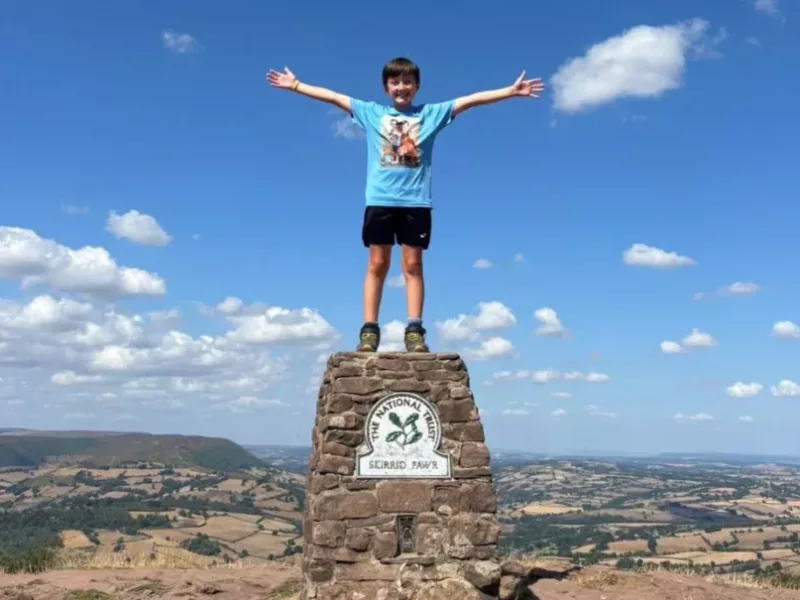 a boy on top of a mountain holding his arms in the air