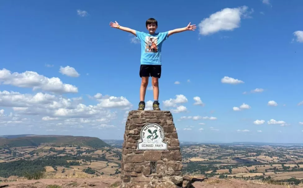 a boy on top of a mountain holding his arms in the air