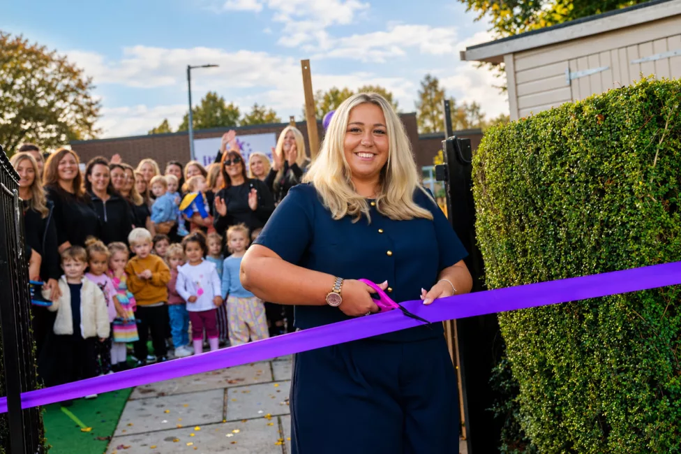 a woman cuts a ribbon in front of a large group of adults and children