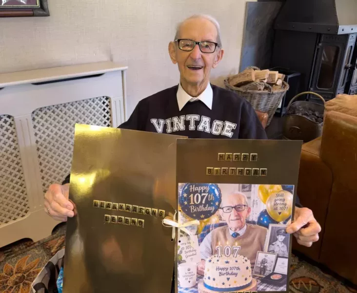 a 107-year-old man sat in a chair smiling holding a birthday card
