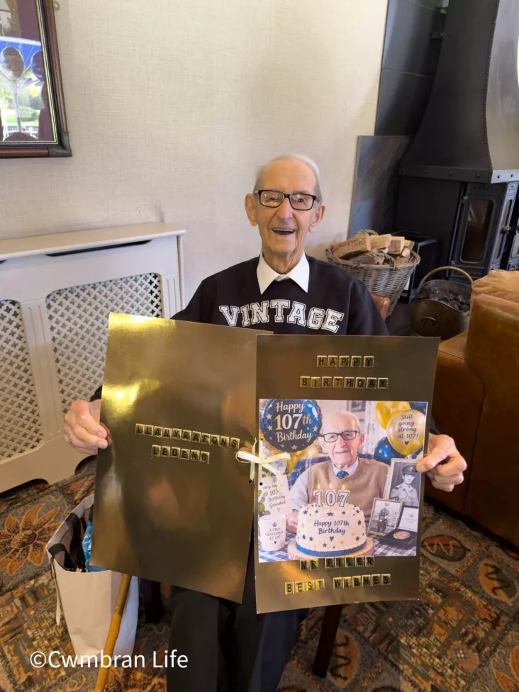 a 107-year-old man sat in a chair smiling holding a birthday card
